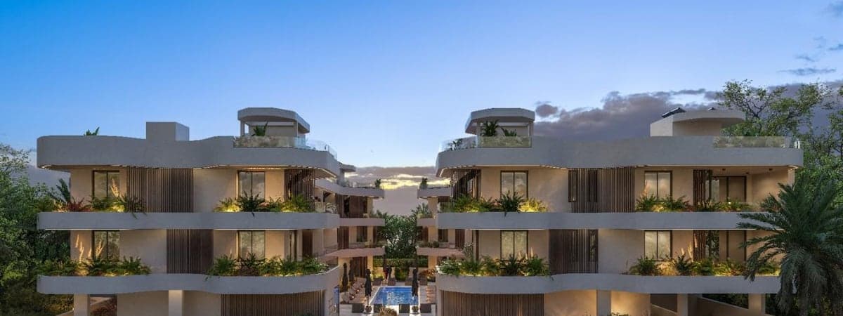 Two white residential buildings at dusk with planted terraces, a pool between them and private rooftops on the top floor